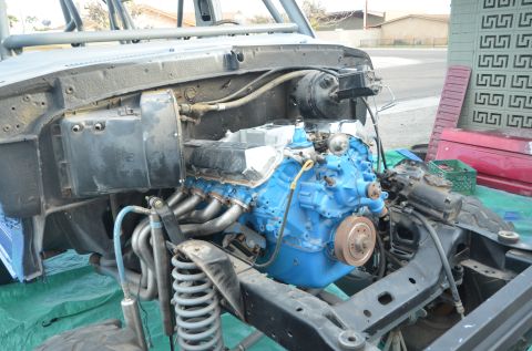 1979 Ford Bronco - The engine bay of a vehicle is shown with a bright blue engine and custom headers, indicating a project in progress.