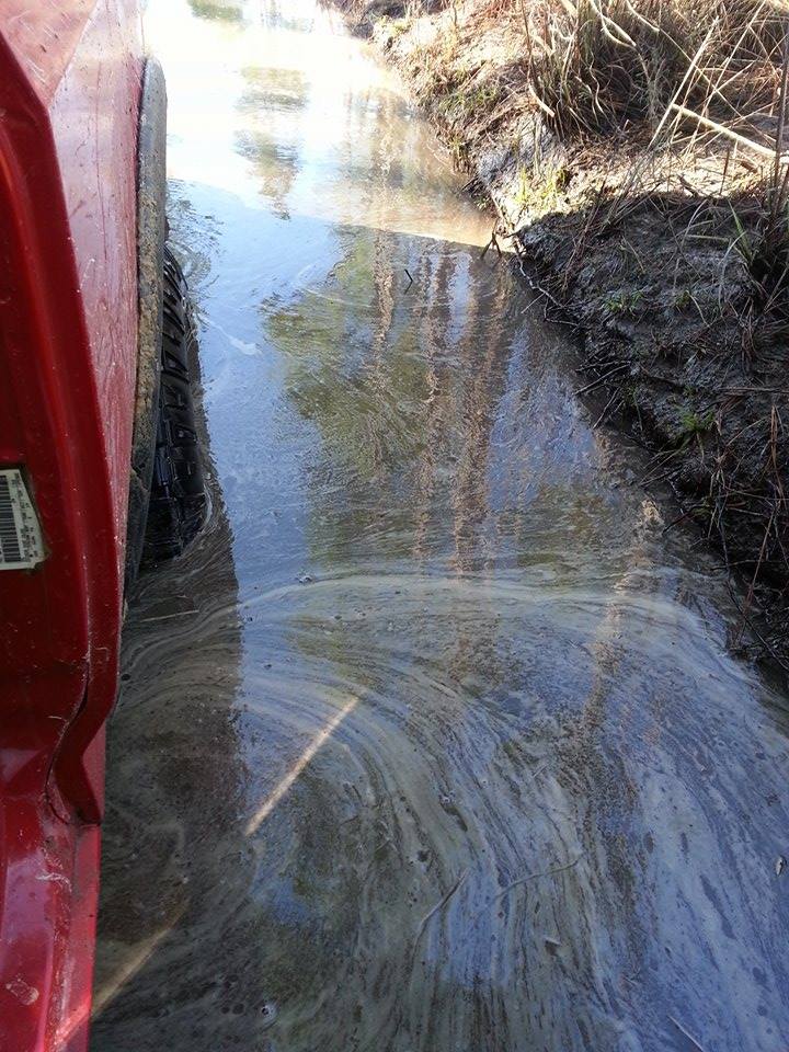 Red vehicle side view driving through murky water and mud
