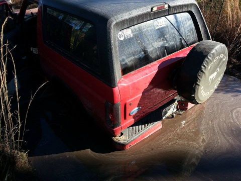 1995 Ford Bronco - This red Ford Bronco is stuck in the mud, with its spare tire cover visible.