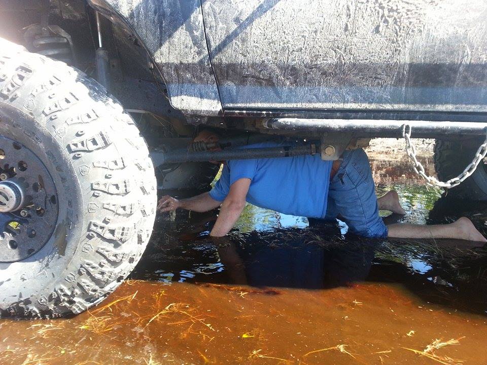 Muddy vehicle undercarriage with a person working beneath it in murky water