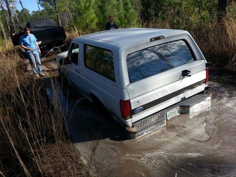 1995 Ford Bronco - Two SUVs are stuck in a muddy, wooded area.
