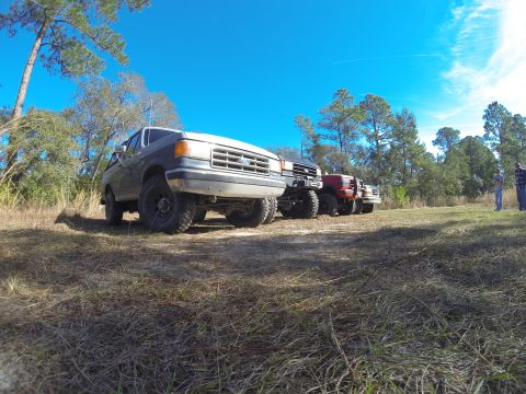 1995 Ford Bronco - Several SUVs, including a 1992 Ford Bronco, are parked in a grassy outdoor area under a clear blue sky.