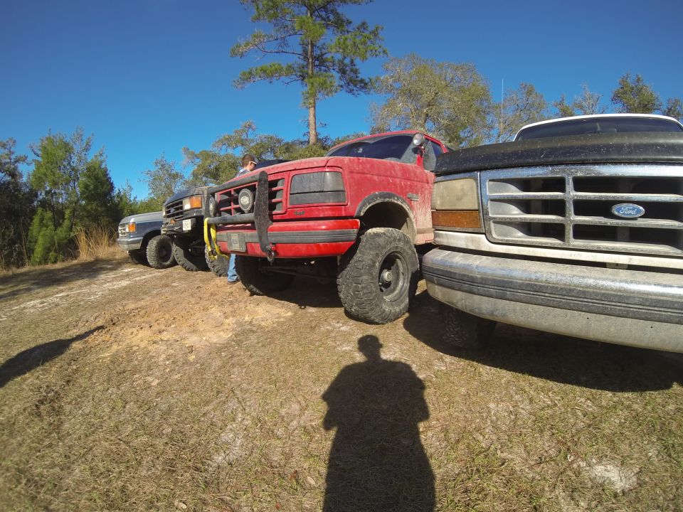Red Ford Bronco with a brush guard and large tires, parked in a grassy, outdoor area