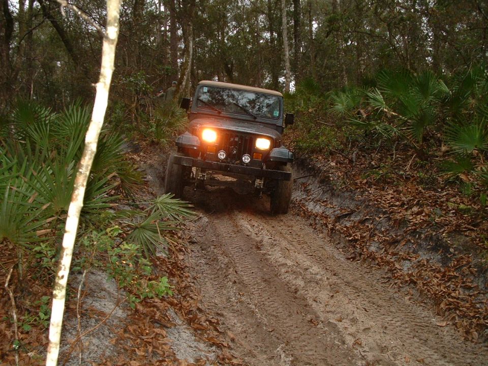 Jeep Wrangler driving up a muddy hill in a wooded area