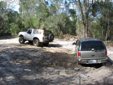 1994 Ford Bronco - Two SUVs navigate a sandy trail surrounded by trees.