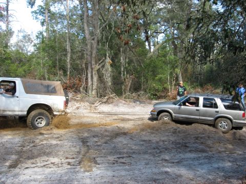 1994 Ford Bronco - Two SUVs are stuck in the mud on a dirt road surrounded by trees.