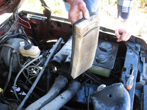 1994 Ford Bronco - A person holds a dirty air filter removed from the engine bay of a vehicle. The engine compartment shows various hoses and reservoirs.