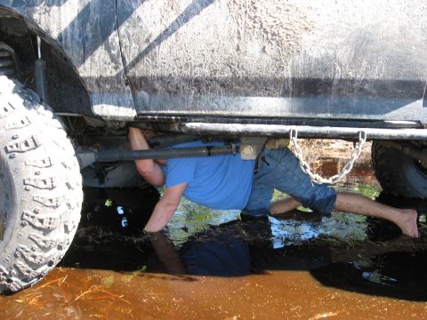 1994 Ford Bronco - A person works on the undercarriage of a vehicle submerged in muddy water.