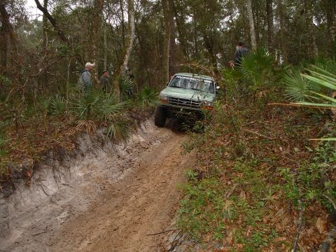 1995 Ford Bronco - A green Ford Bronco navigates a challenging muddy off-road course surrounded by dense foliage.