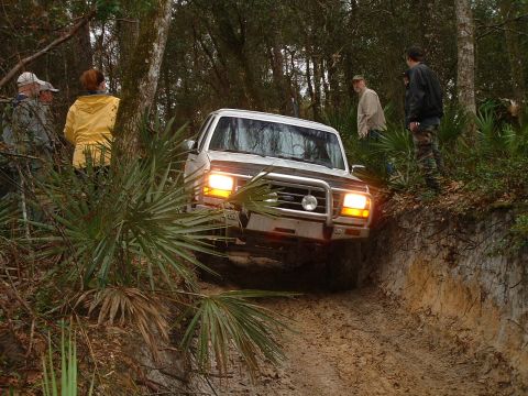 1995 Ford Bronco - Ford Bronco navigates a challenging muddy off-road course with onlookers present.