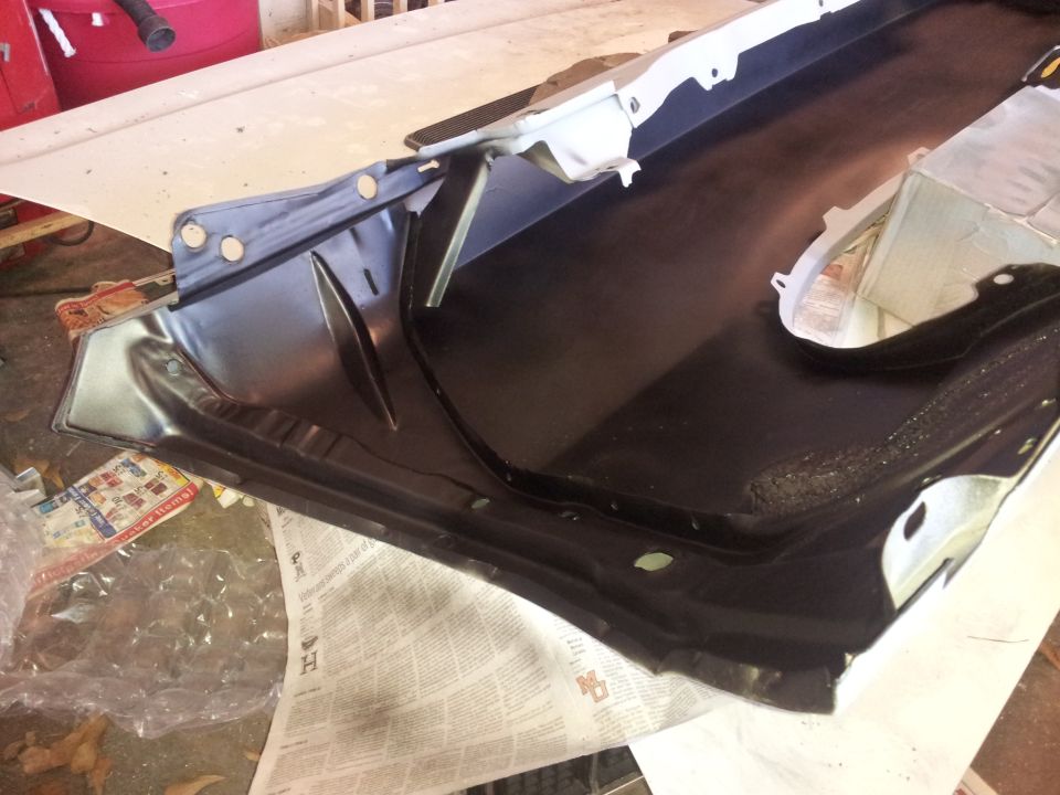 black metal car part, possibly a fender well or undercarriage piece, on a workbench