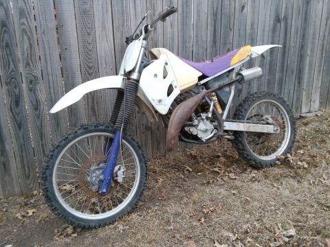 1986 Ford Bronco - This dirt bike is parked outdoors next to a weathered wooden fence.