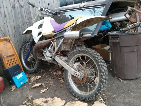 1986 Ford Bronco - A dirt bike sits in an outdoor storage area, partially obscured by debris and next to other items.