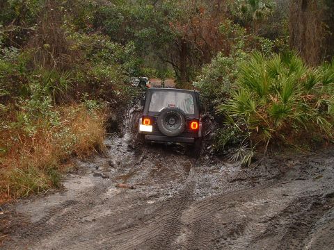 1995 Ford Bronco - A black SUV struggles through a muddy off-road path, with another vehicle visible ahead.