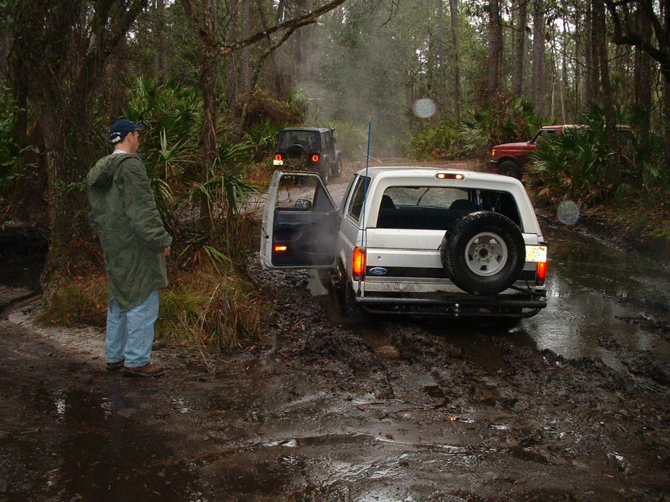 1995 Ford Bronco stuck in mud with other vehicles behind it on a wooded trail