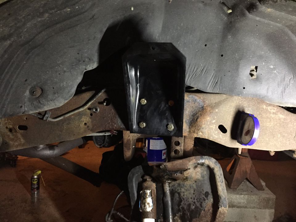 Vehicle frame with new black bracket bolted to rusty crossmember, blue bushing on jack stand