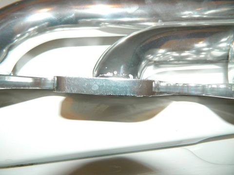1979 Ford Bronco - Close-up of polished chrome tube exhaust headers showing a welded mounting flange between primary tubes.
