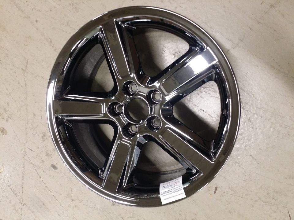 Five-spoke dark chrome alloy wheel lying face-up on concrete floor