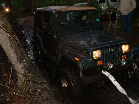 1995 Ford Bronco - A Jeep Wrangler TJ navigates a muddy trail with trees and another vehicle in the background.