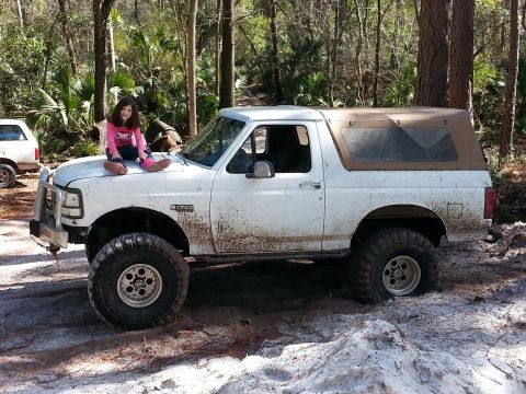 1992 Ford Bronco - A girl sits on the hood of a white 1992 Ford Bronco, which appears to be off-roading.