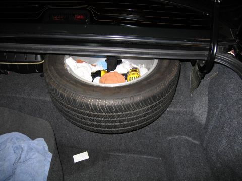 1985 Ford Crown Victoria LTD - The trunk of a car contains a spare tire and various items, including cloths and a yellow object.