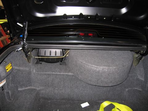 1985 Ford Crown Victoria LTD - The trunk of a black car is shown, revealing the spare tire compartment and aftermarket subwoofer.