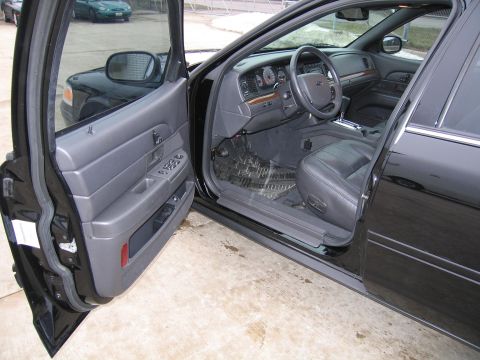 1985 Ford Crown Victoria LTD - Interior view of a black sedan with the driver's door open, revealing the dashboard and seats.