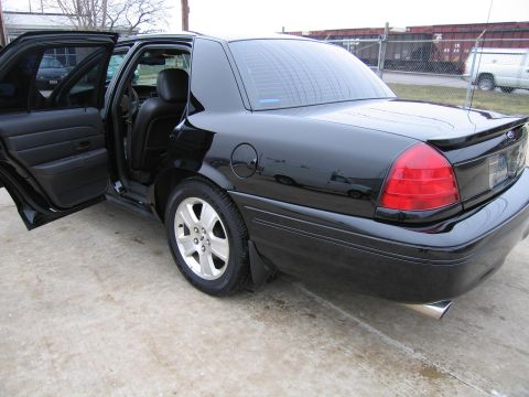 1985 Ford Crown Victoria LTD - This black sedan, seen from the rear 3/4 angle with its doors open, appears to be a 2005 model based on its body style.