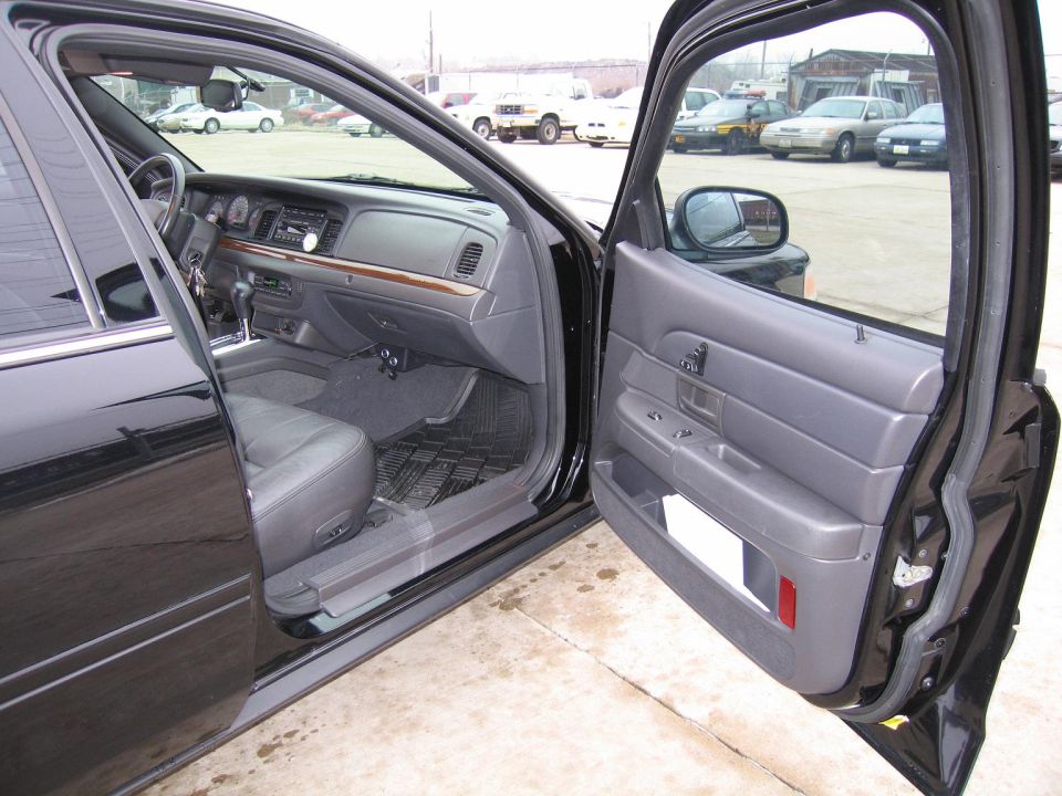 Interior of a black Ford Crown Victoria, showing the dashboard, driver's seat, and open passenger door