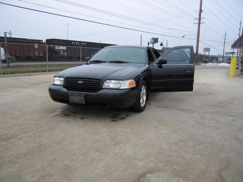 1985 Ford LTD Crown Victoria - A black Ford Crown Victoria is parked with its driver's door ajar.