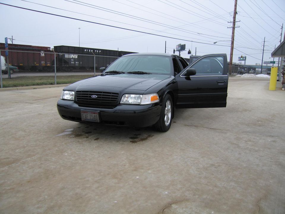 Black Ford Crown Victoria with driver's door open, parked on concrete