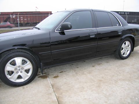 1985 Ford LTD Crown Victoria - Side profile of a black sedan with tinted windows and chrome trim. The vehicle is parked on a concrete surface.