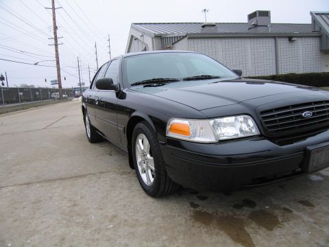 1985 Ford LTD Crown Victoria - A black Ford Crown Victoria is parked on a concrete surface with a building and utility poles visible in the background.