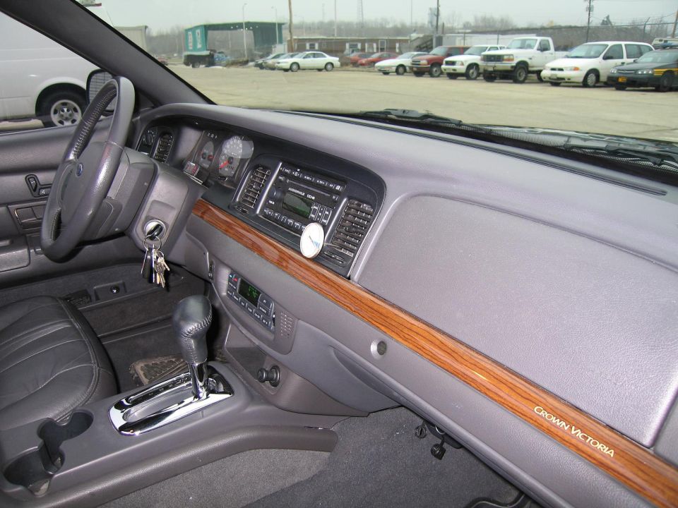 Interior shot of a Ford Crown Victoria showing the dashboard, steering wheel, and gear shifter. Wood trim runs across the dash