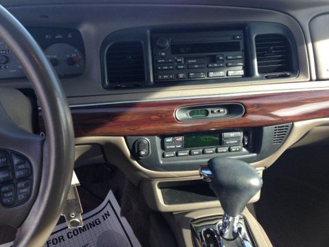 1995 Mercury Grand Marquis - The dashboard of a car features wood grain trim, a digital clock, and an audio system display.