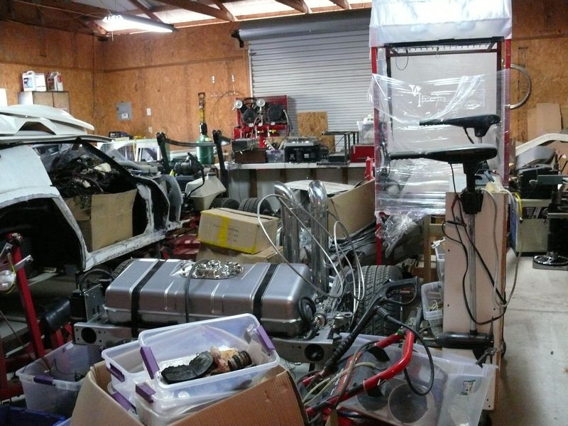 Disassembled vehicle body and parts in a cluttered garage, including a fuel tank and engine components