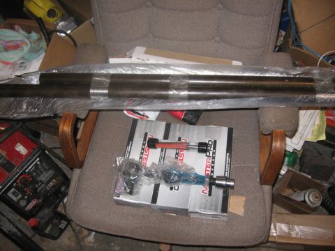 1988 Ford Bronco - A driveshaft and tie rod ends are visible on a chair, surrounded by various items.