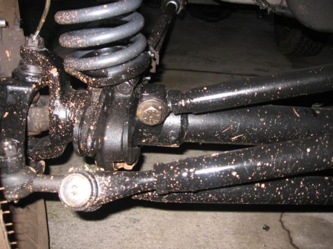 1988 Ford Bronco - Close-up view of the front suspension components, including tie rods and a coil spring, heavily coated in mud.