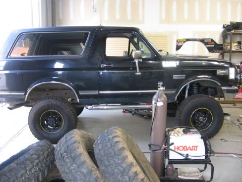1988 Ford Bronco - A black Ford Bronco is shown in a garage setting, with spare tires and a welding machine visible.