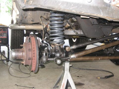 1988 Ford Bronco - Front suspension and brake assembly of a truck, with a welding machine visible.