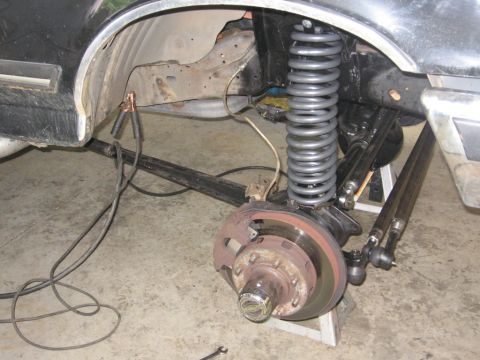 1988 Ford Bronco - Close-up of a vehicle's front suspension and brake components, with jumper cables attached.