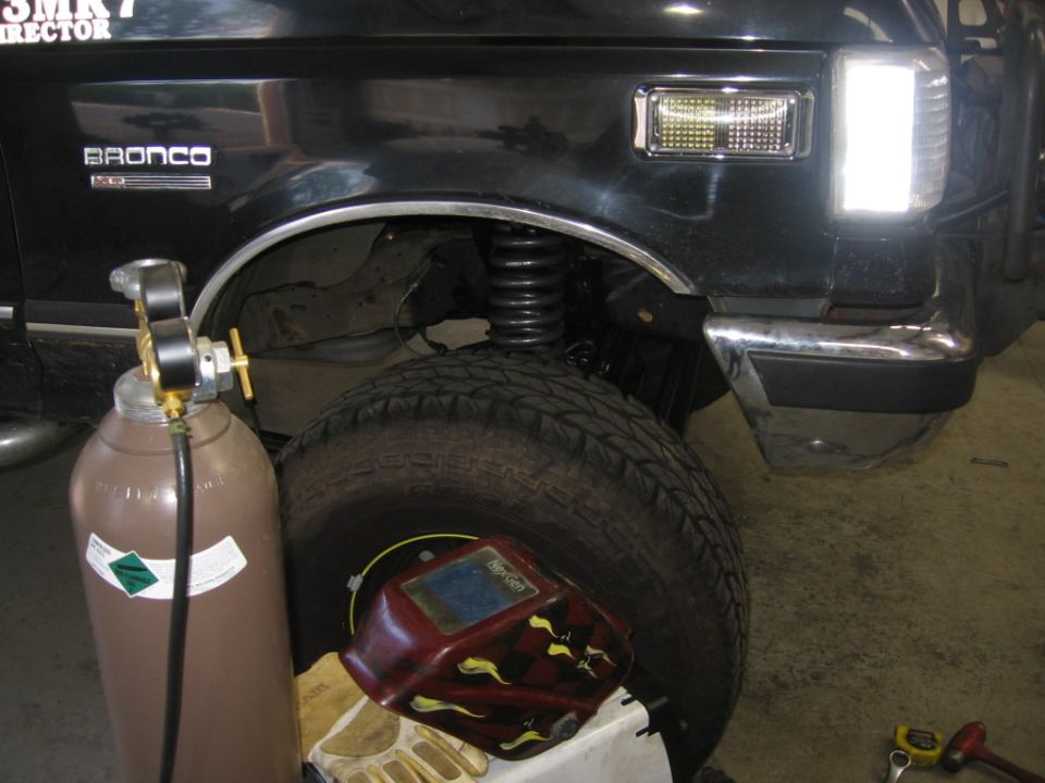 Black 1988 Ford Bronco front fender and tire, with welding equipment nearby