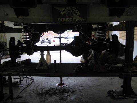 1988 Ford Bronco - The underside of a vehicle is shown being worked on, with a white truck in the background.