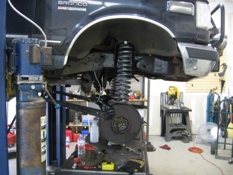 1988 Ford Bronco - The front suspension of a 1988 Ford Bronco is visible as it's lifted for service in a garage setting.