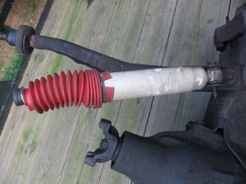 1988 Ford Bronco - Close-up of a vehicle's suspension component, a shock absorber with a red boot and a U-joint, resting on a wooden surface.