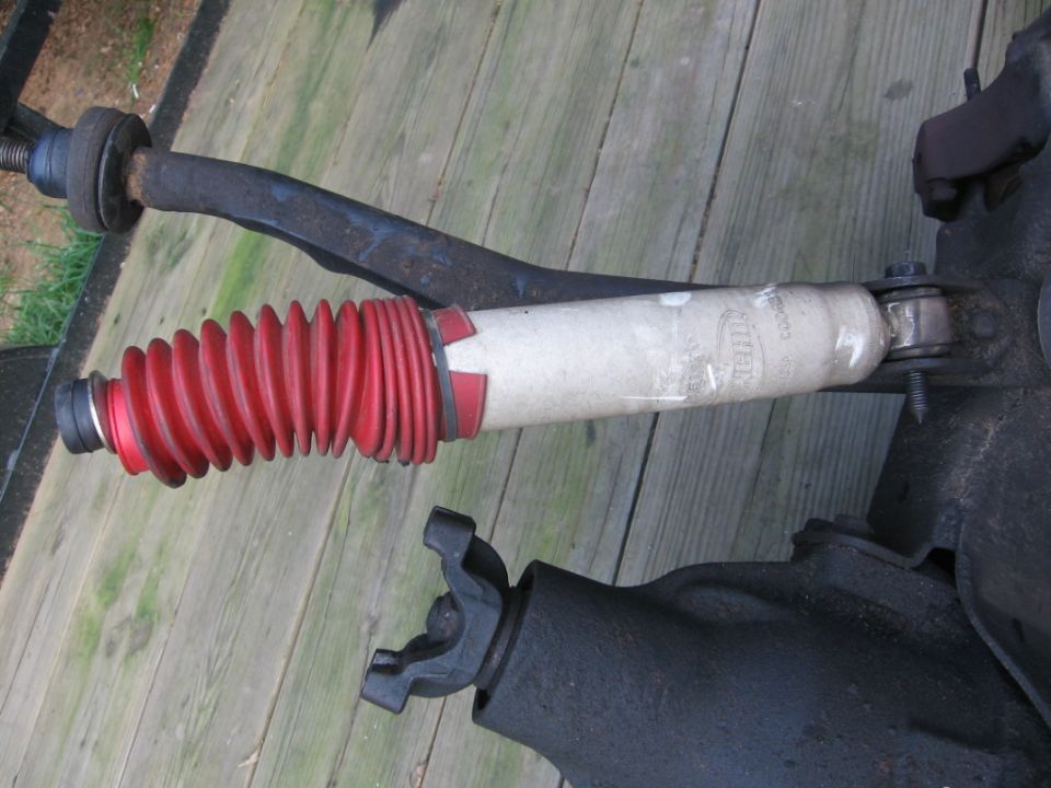 Shock absorber with red boot and U-joint on wooden surface