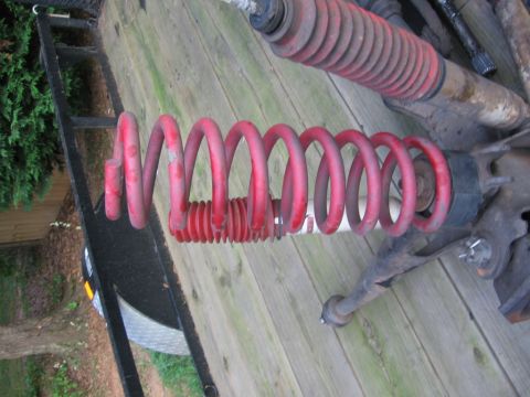 1988 Ford Bronco - Close-up of red coil spring and other suspension parts, likely for a vehicle, resting on a wooden deck.