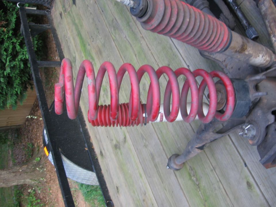 Red coil spring and suspension components on a wooden surface