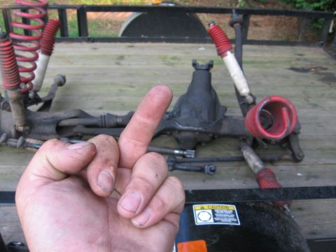 1988 Ford Bronco - Front axle assembly with red springs and shocks, with a hand obscuring part of the view.