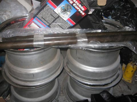 1988 Ford Bronco - A collection of automotive parts, including wheels and a metal bar, are stored together with a product box.